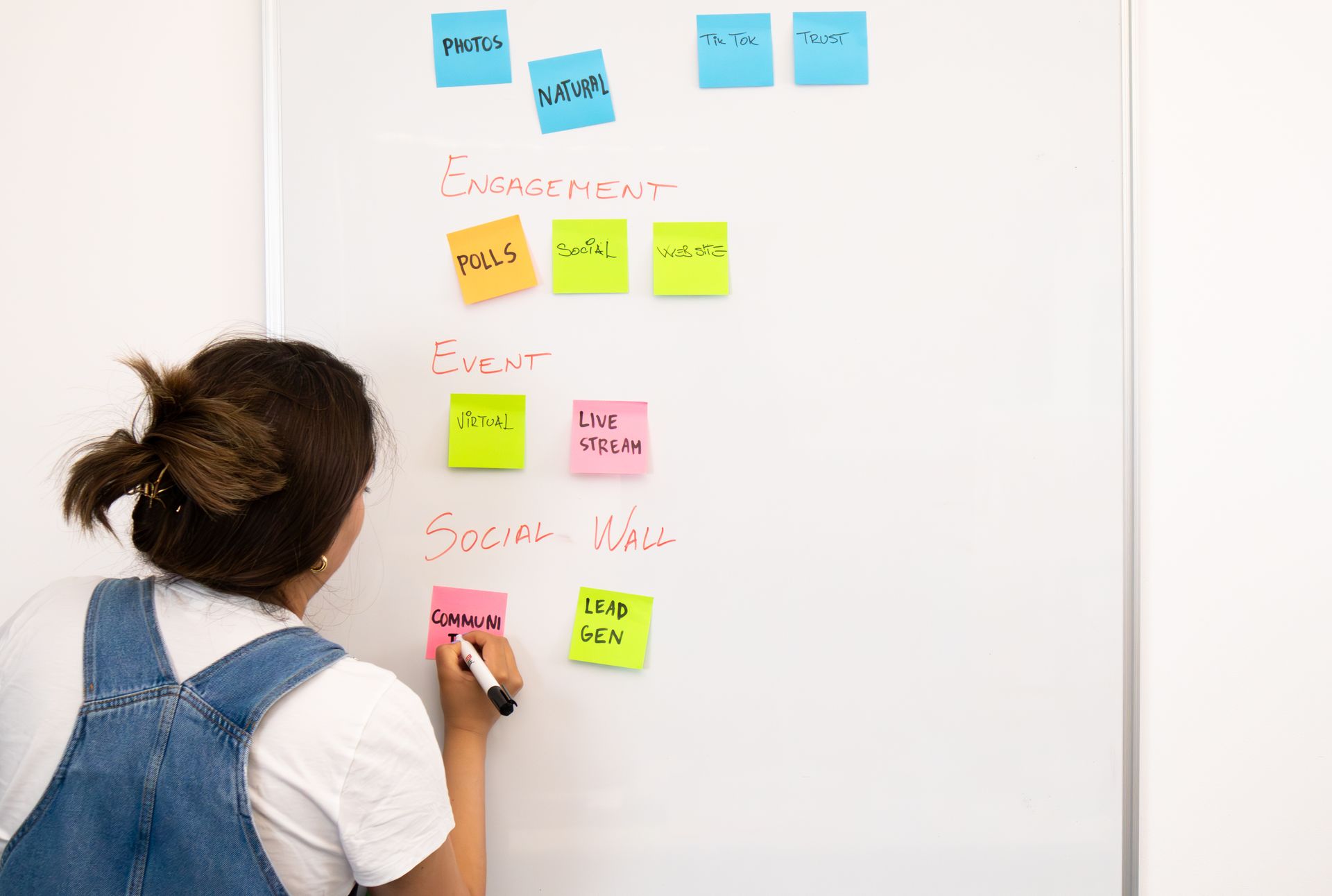 A woman organizing notes on a whiteboard with colorful sticky notes in an office setting.