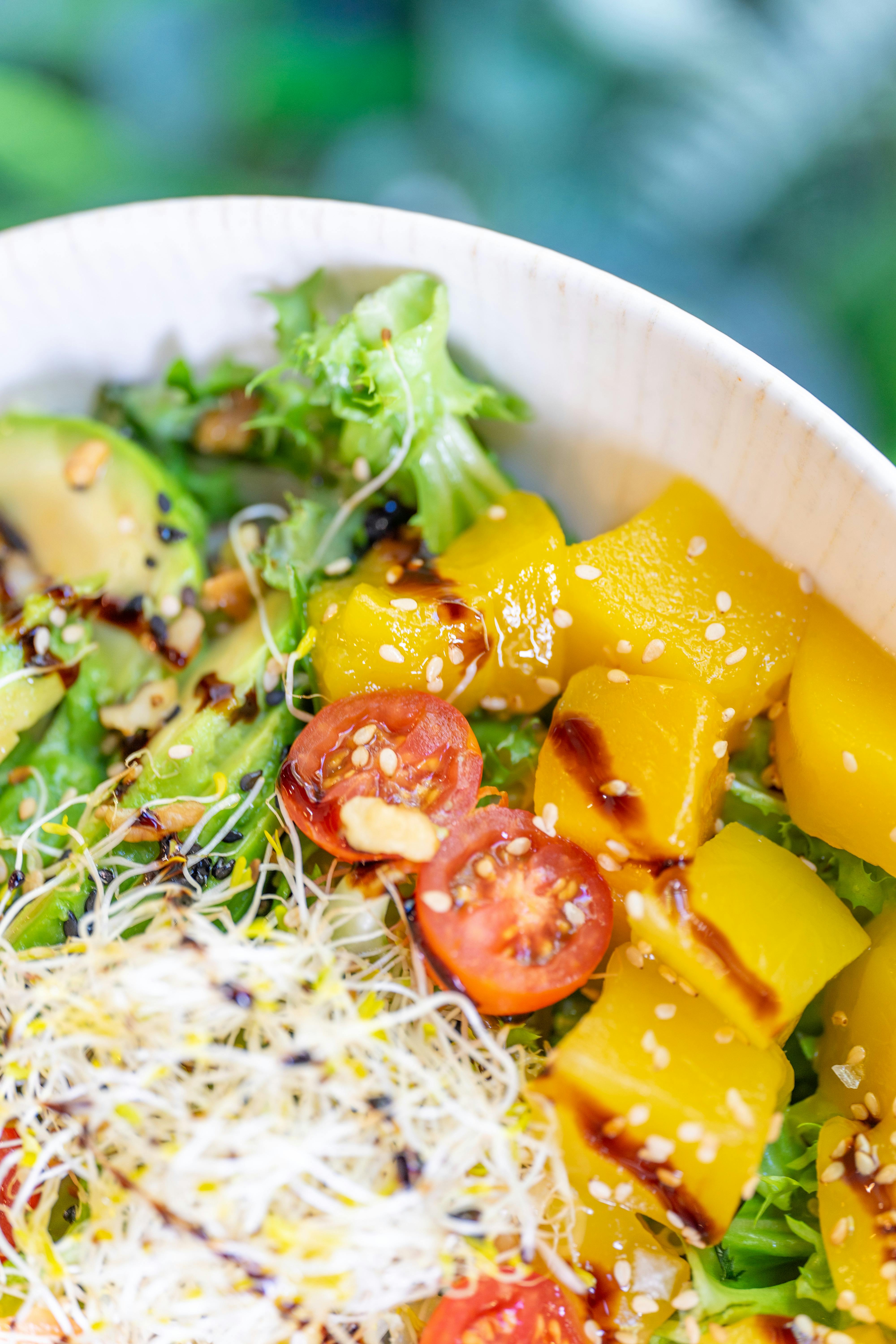 A bowl of salad with avocado, tomatoes and sprouts