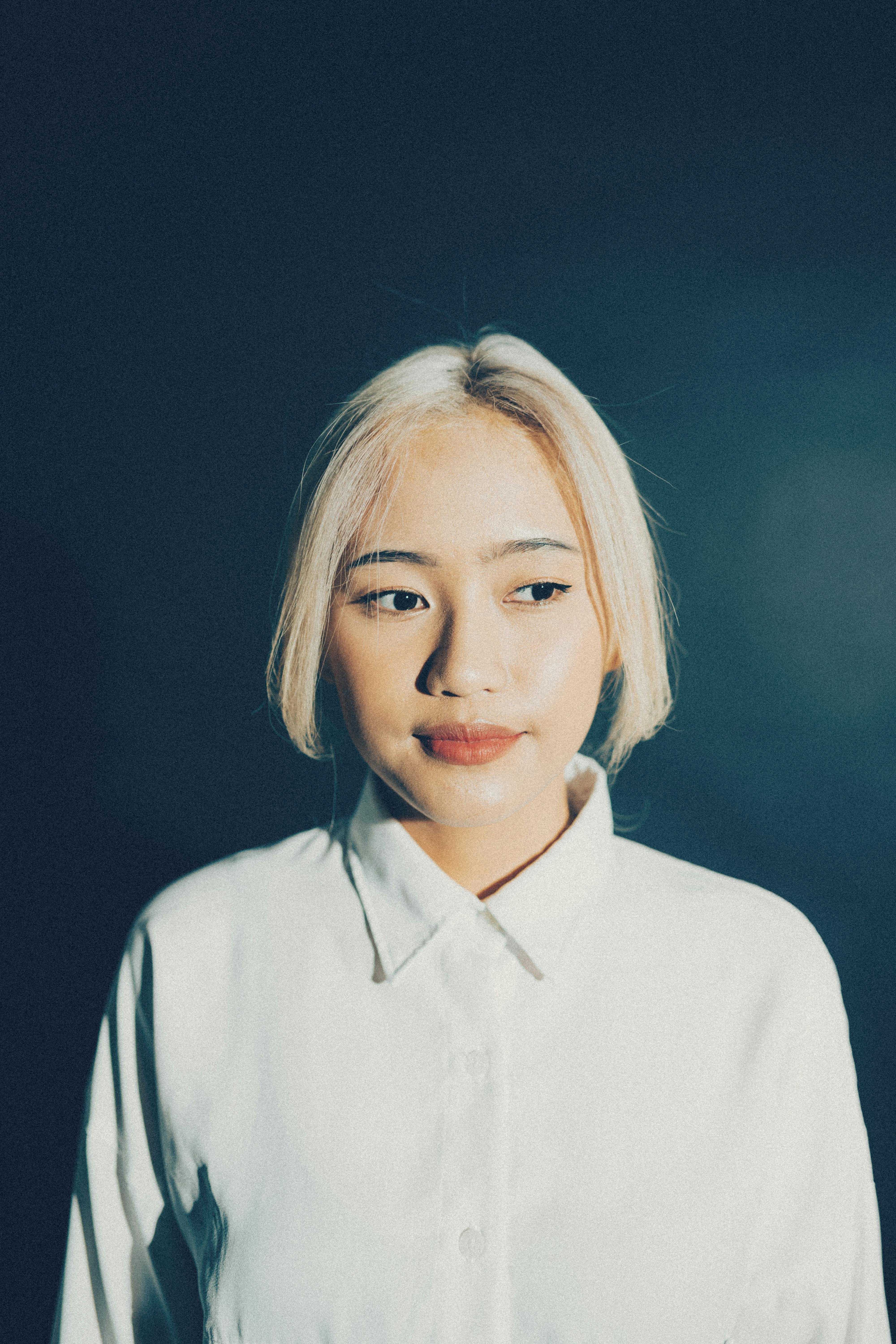 A peaceful portrait of a young woman with light hair wearing a white shirt against a dark background.