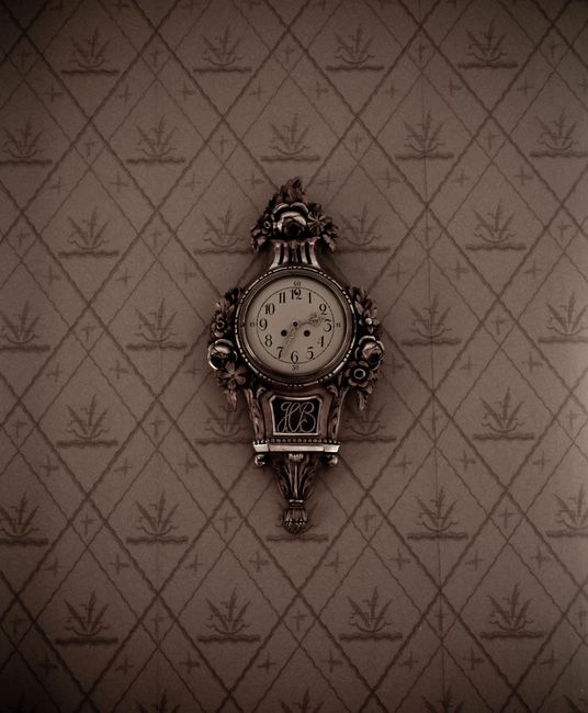 Elegant vintage wall clock with ornate design on patterned wallpaper.