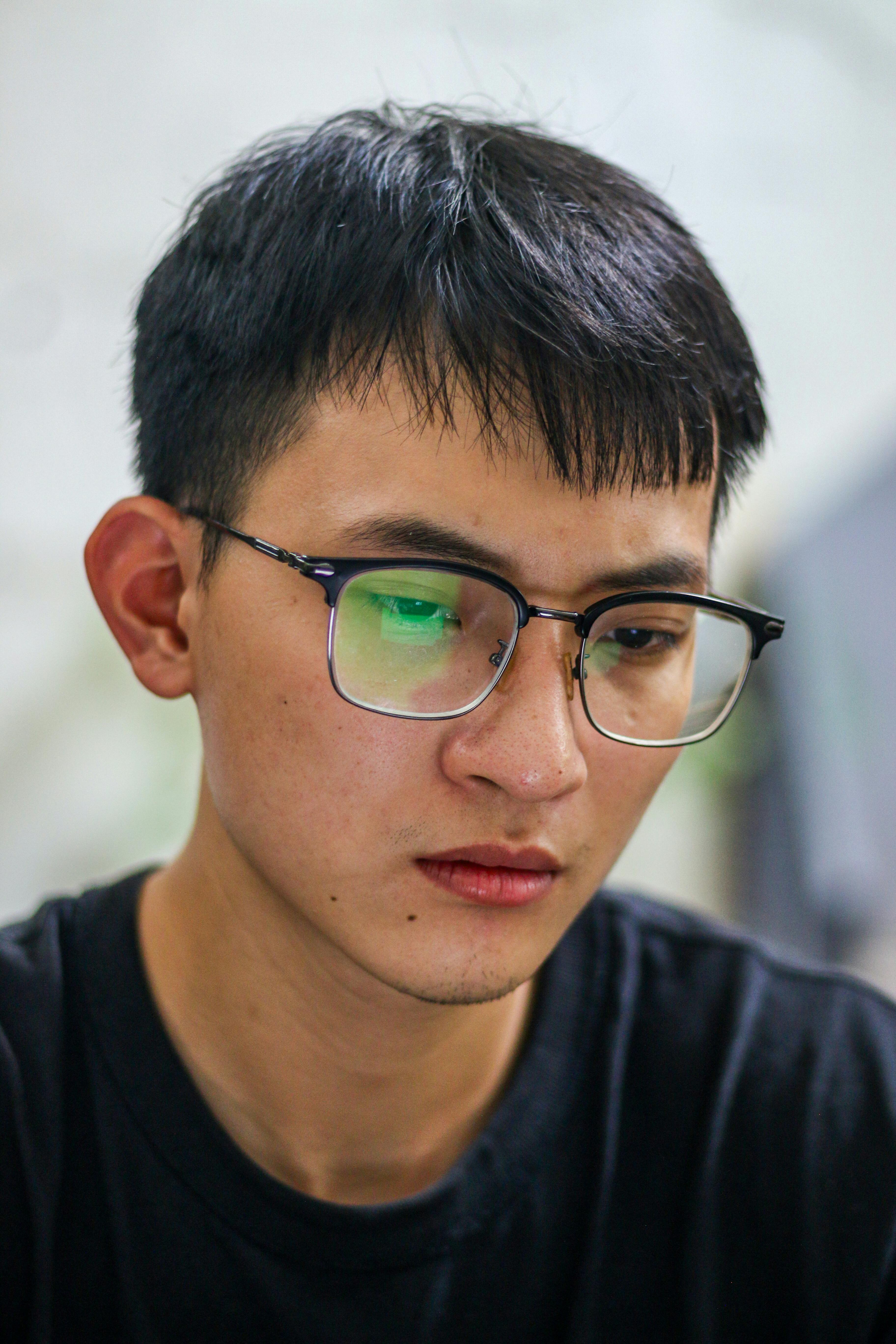 Close-up of a young man with glasses deeply focused on a task indoors.