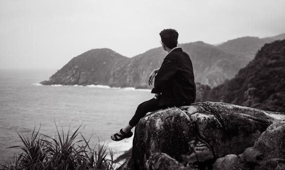 A man sits on a rock overlooking the misty mountain sea, reflecting in solitude.
