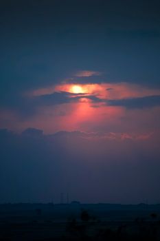 A breathtaking sunset with vibrant orange and pink hues, partially obscured by clouds against a darkening sky.