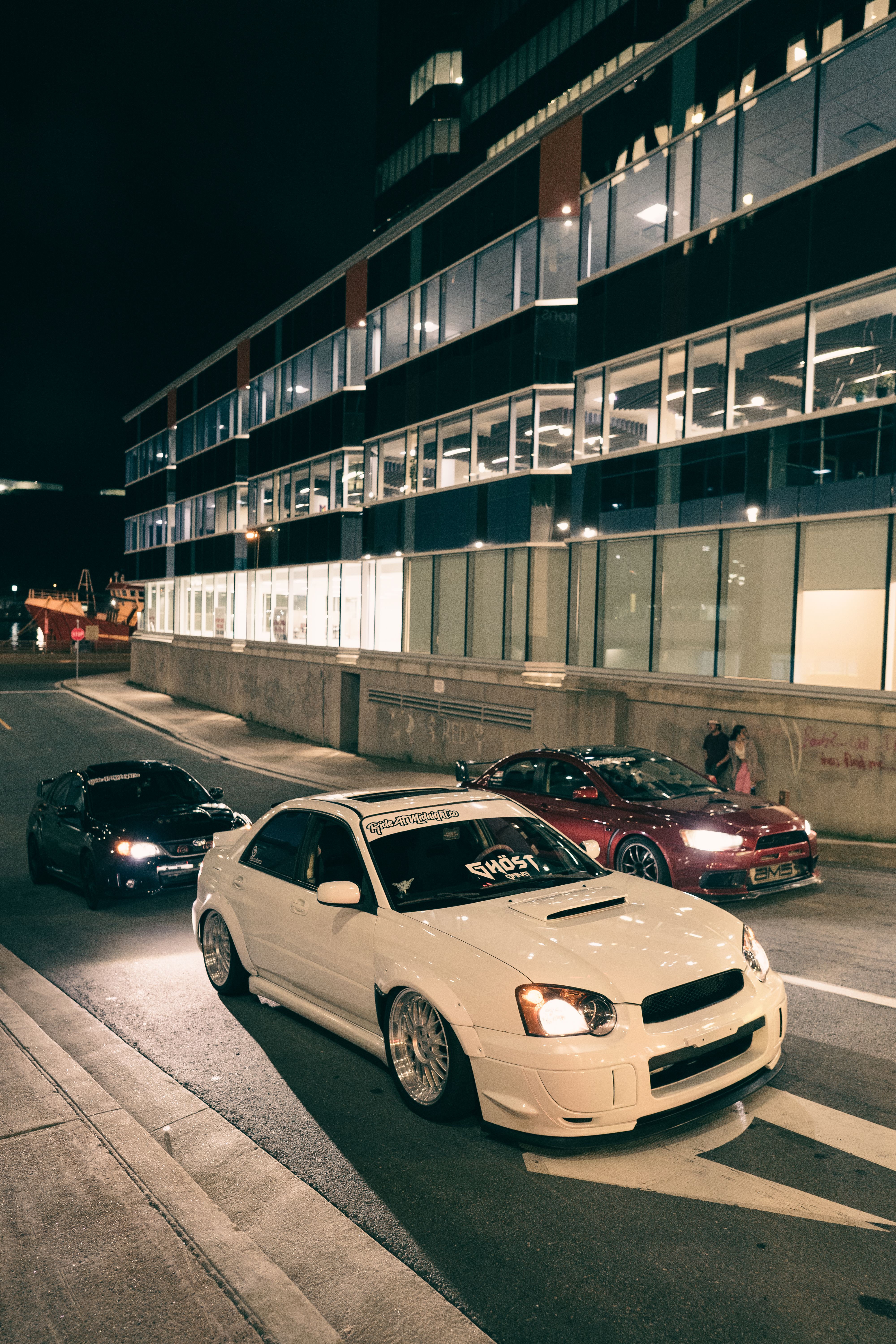 Modern cars parked on an urban street at night, showcasing luxury and style.
