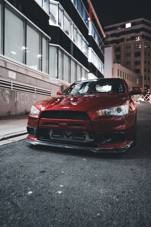 Free Red sports car parked on a nighttime city street, embodying speed and style. Stock Photo