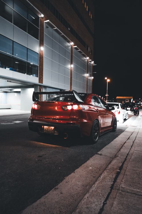 Free Dynamic view of a red sports car on an urban street at night, showcasing city lights. Stock Photo
