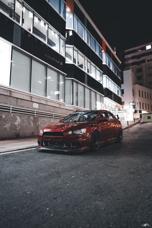 Free A striking red car parked on a city street at night, showcasing urban architecture. Stock Photo