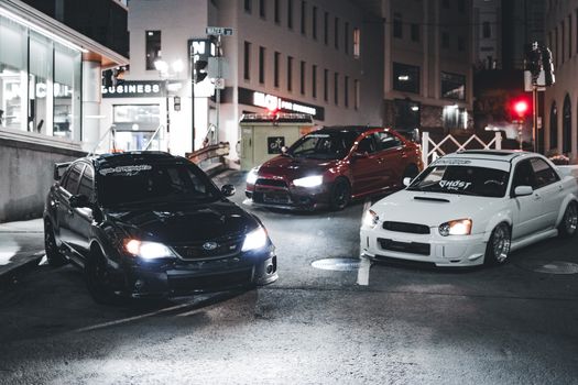 Three modified cars parked on an urban street at night showcasing automotive style.