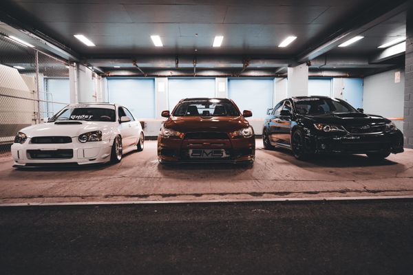 Três carros esportivos elegantes estacionados lado a lado em um ambiente de garagem urbana bem iluminado.