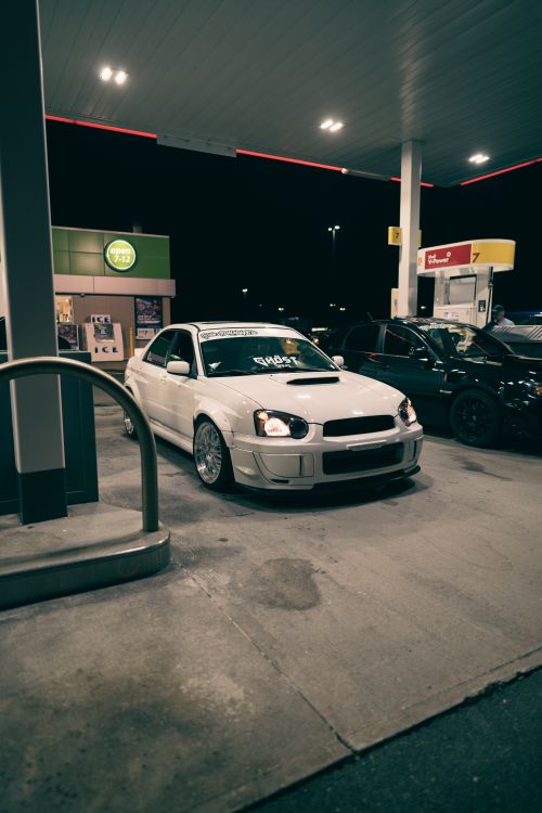 Free White sports car parked at a gas station at night under bright lights. Stock Photo