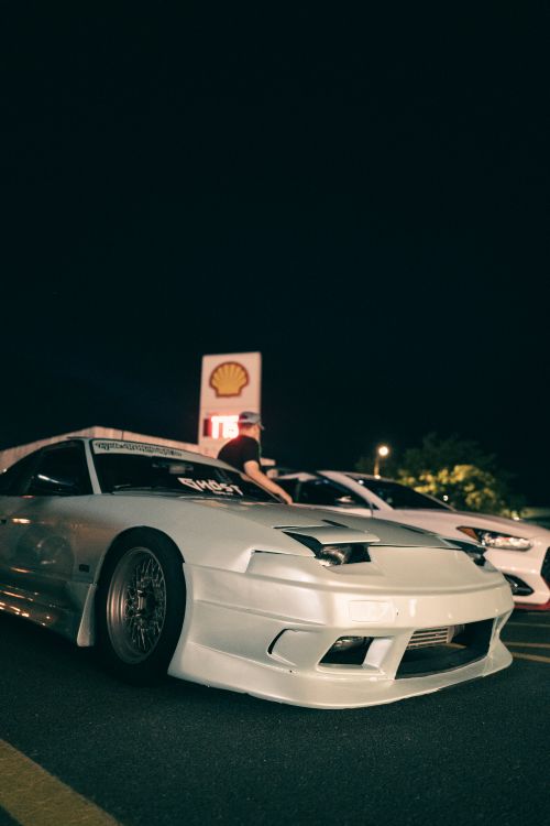 Free Low-angle view of a white sports car parked at night near a gas station, capturing a sense of adventure. Stock Photo