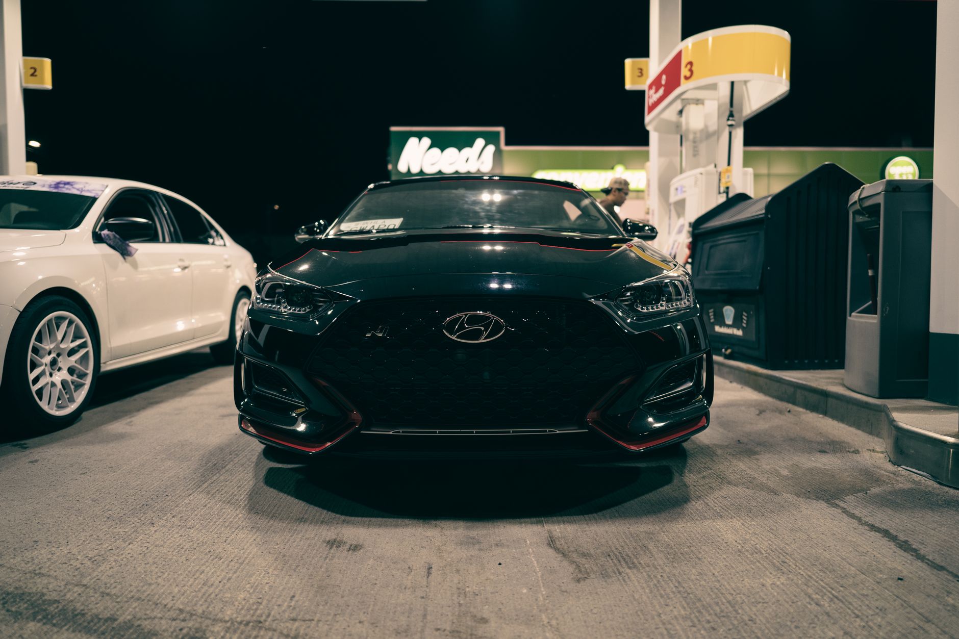 Front view of a black Hyundai at a gas station at night, illuminated scene.