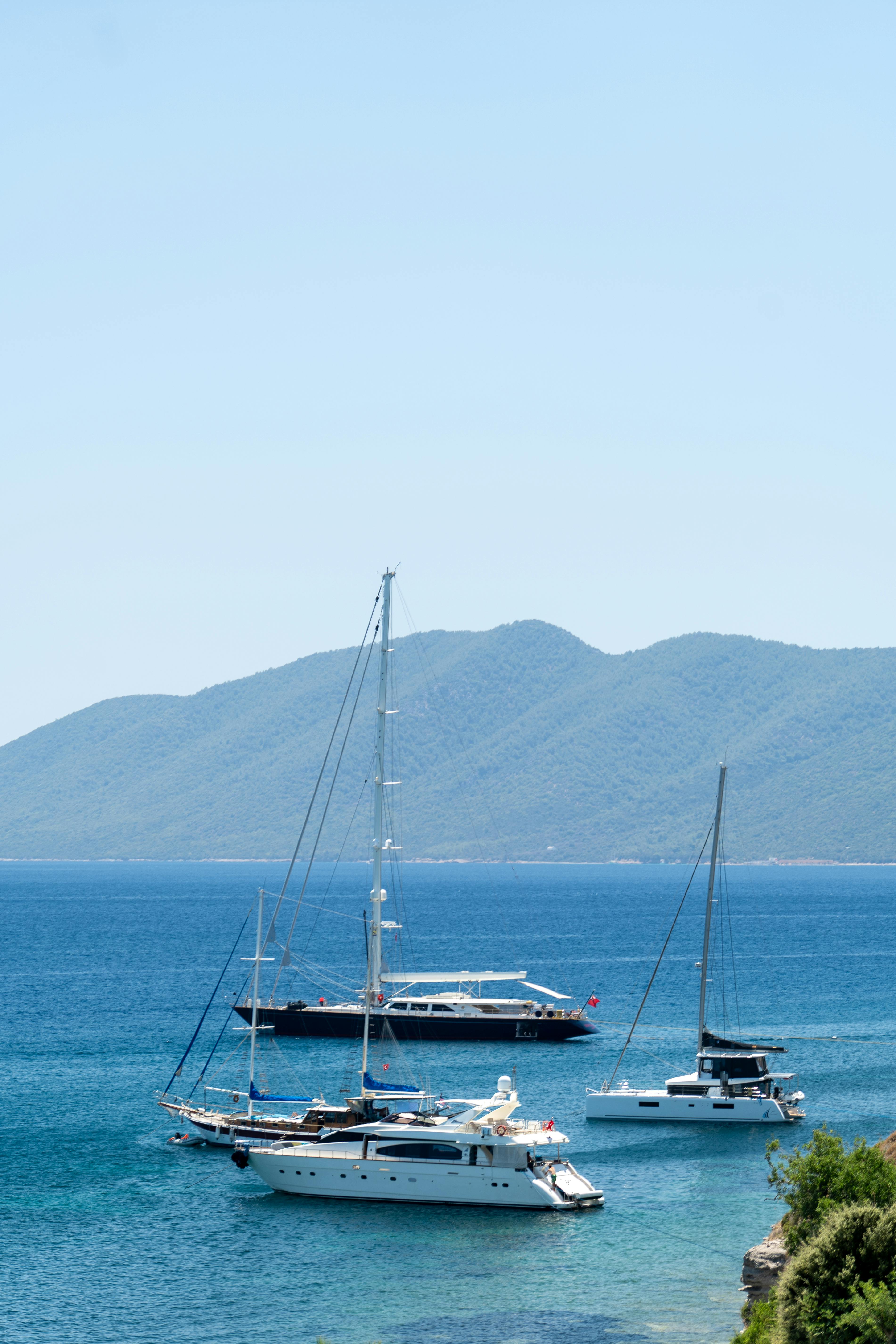 Free Elegant yachts resting in a serene bay with mountains in the background, perfect for luxurious getaways. Stock Photo