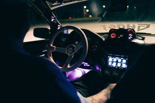 Free A car interior at night with a brightly lit dashboard and steering wheel, showcasing modern technology. Stock Photo