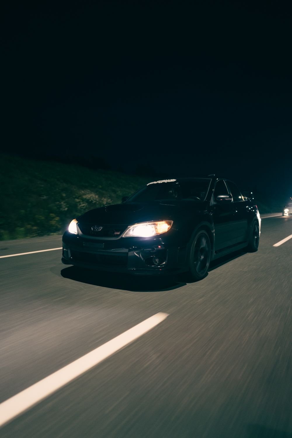A black car driving down the road at night · Free Stock Photo