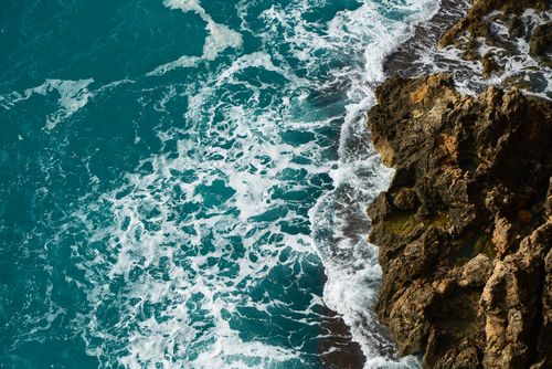 Free Aerial view of waves crashing against rocky coastline, showcasing the sea's natural beauty. Stock Photo