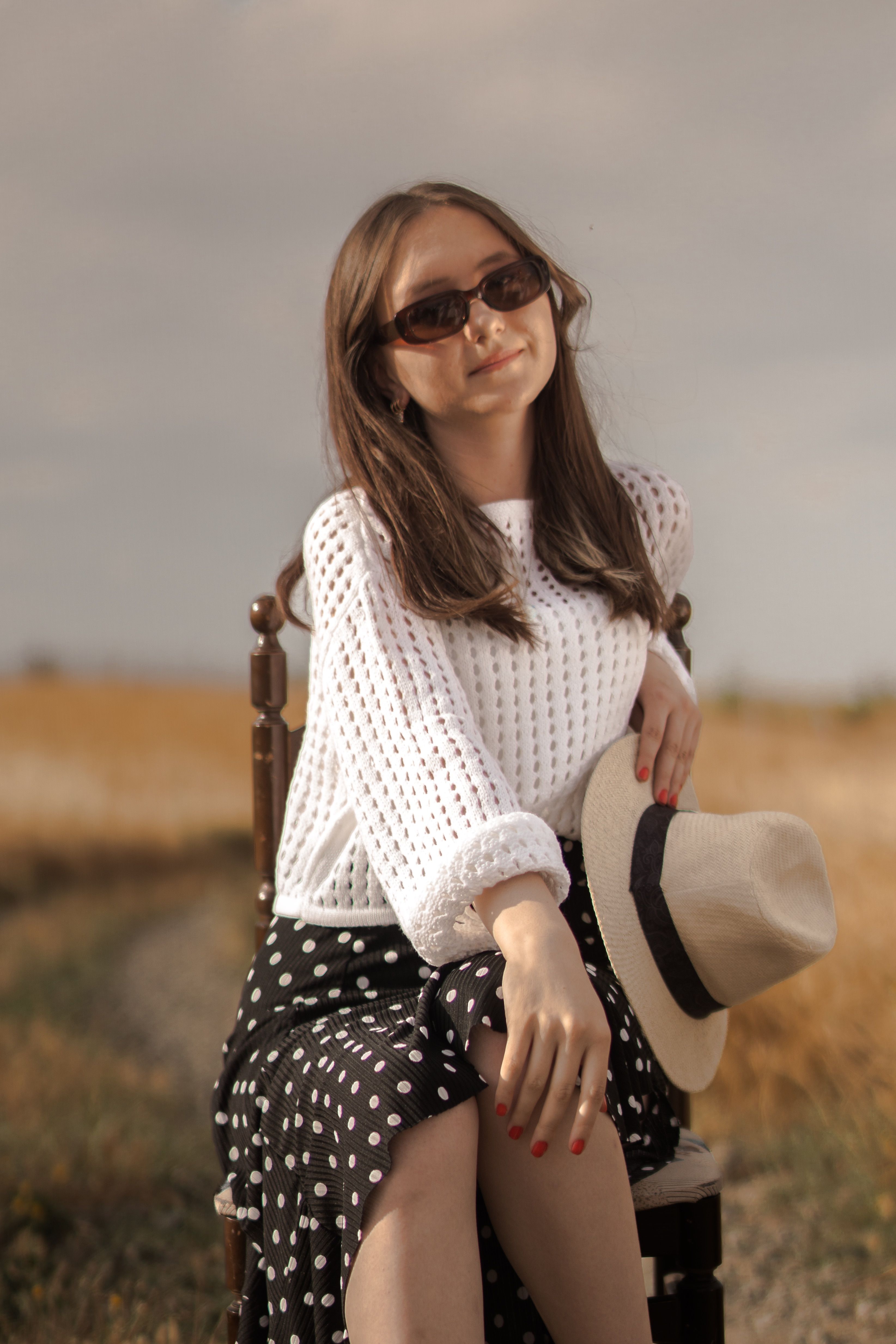 A woman in a hat and polka dot dress sitting on a chair · Free Stock Photo