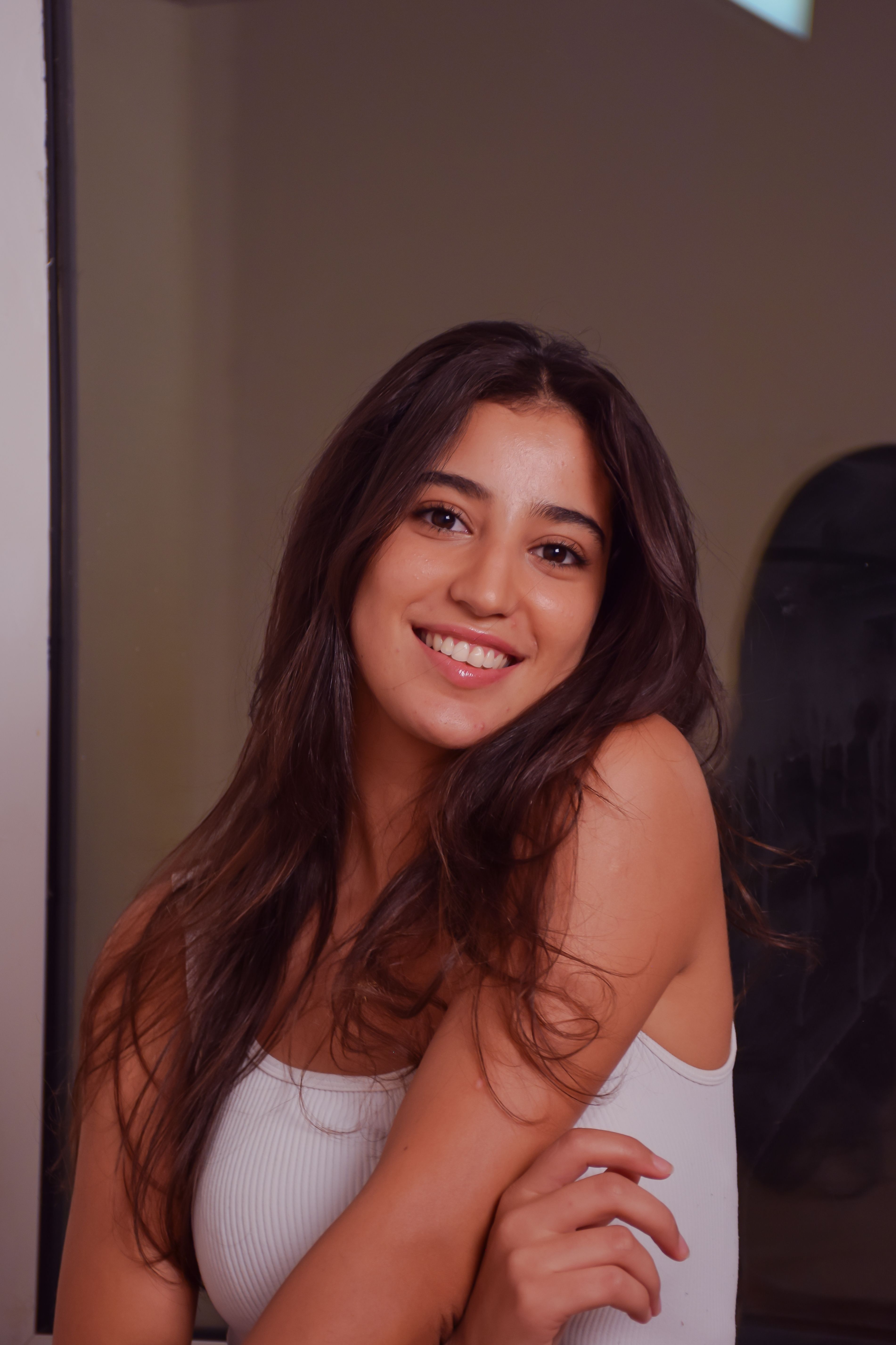 A cheerful woman with long brunette hair smiling indoors in Tunis, Tunisia.