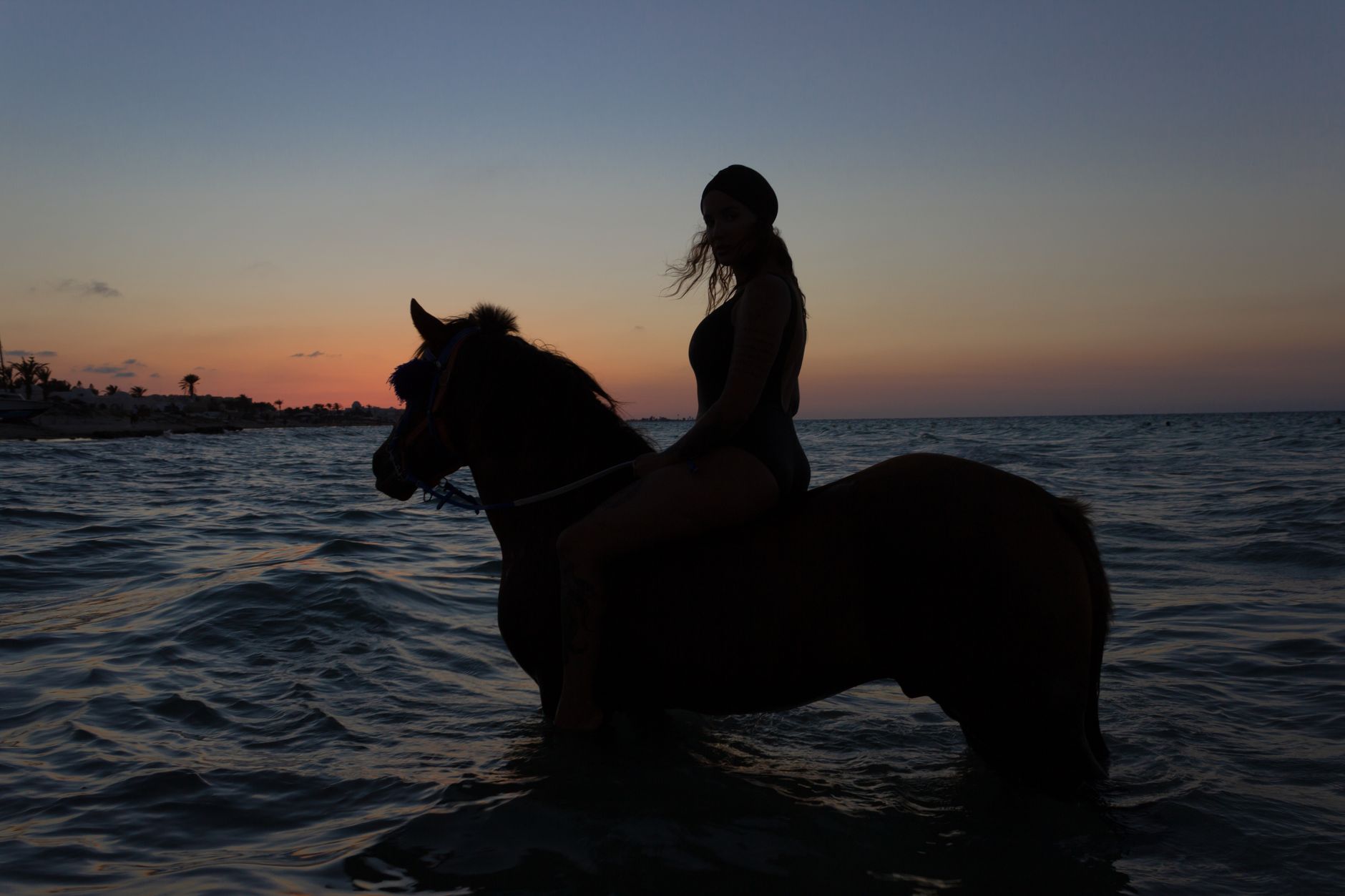 Woman riding horse at ocean sunset