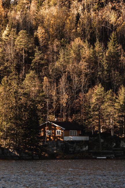 A charming cabin nestled by a forested lake, capturing the serene beauty of autumn.