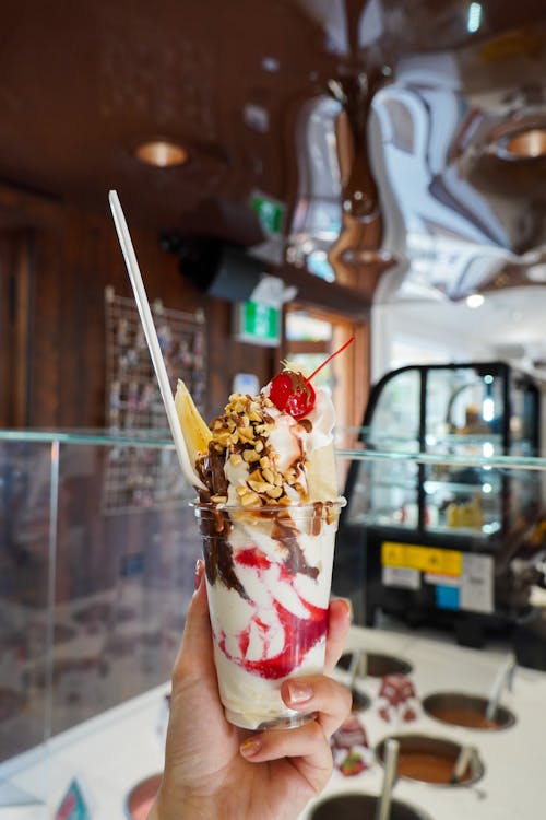 A person holding up a dessert with ice cream and toppings