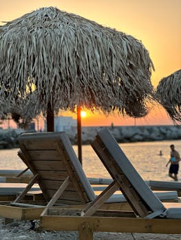 Cozy beach scene with straw umbrellas and sunbeds at sunset, perfect for vacation themes.