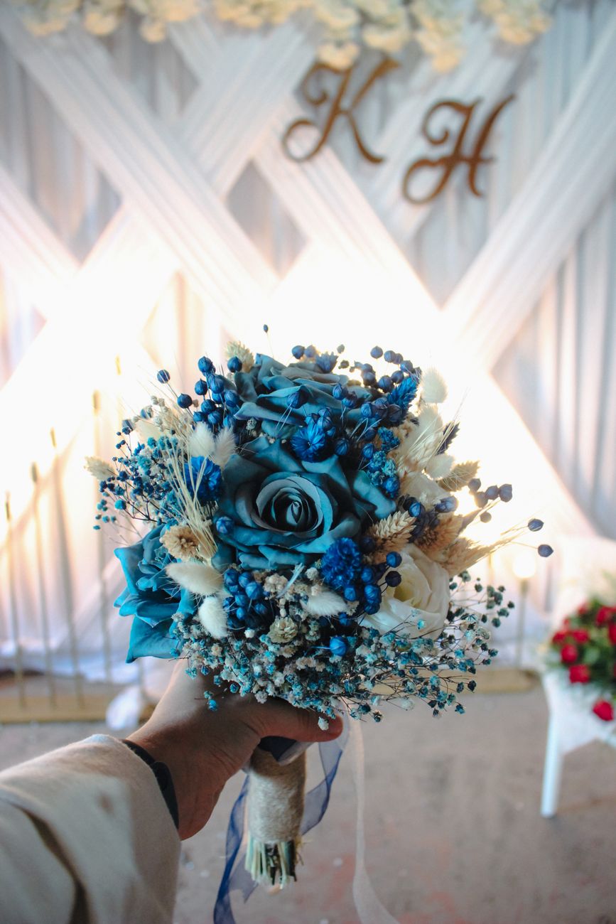 A close-up of a vibrant blue wedding bouquet held indoors against a decorative backdrop.