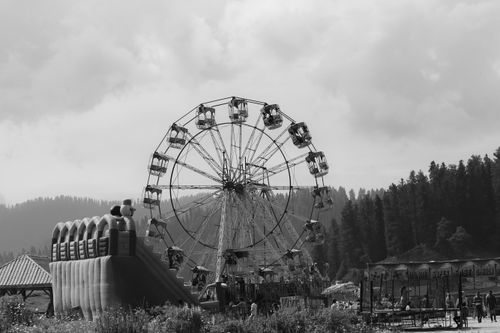 Free Black and white photo of a Ferris wheel at an outdoor fairground with people and trees. Stock Photo