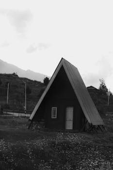 A black and white image of a solitary A-frame cabin in a peaceful rural setting.