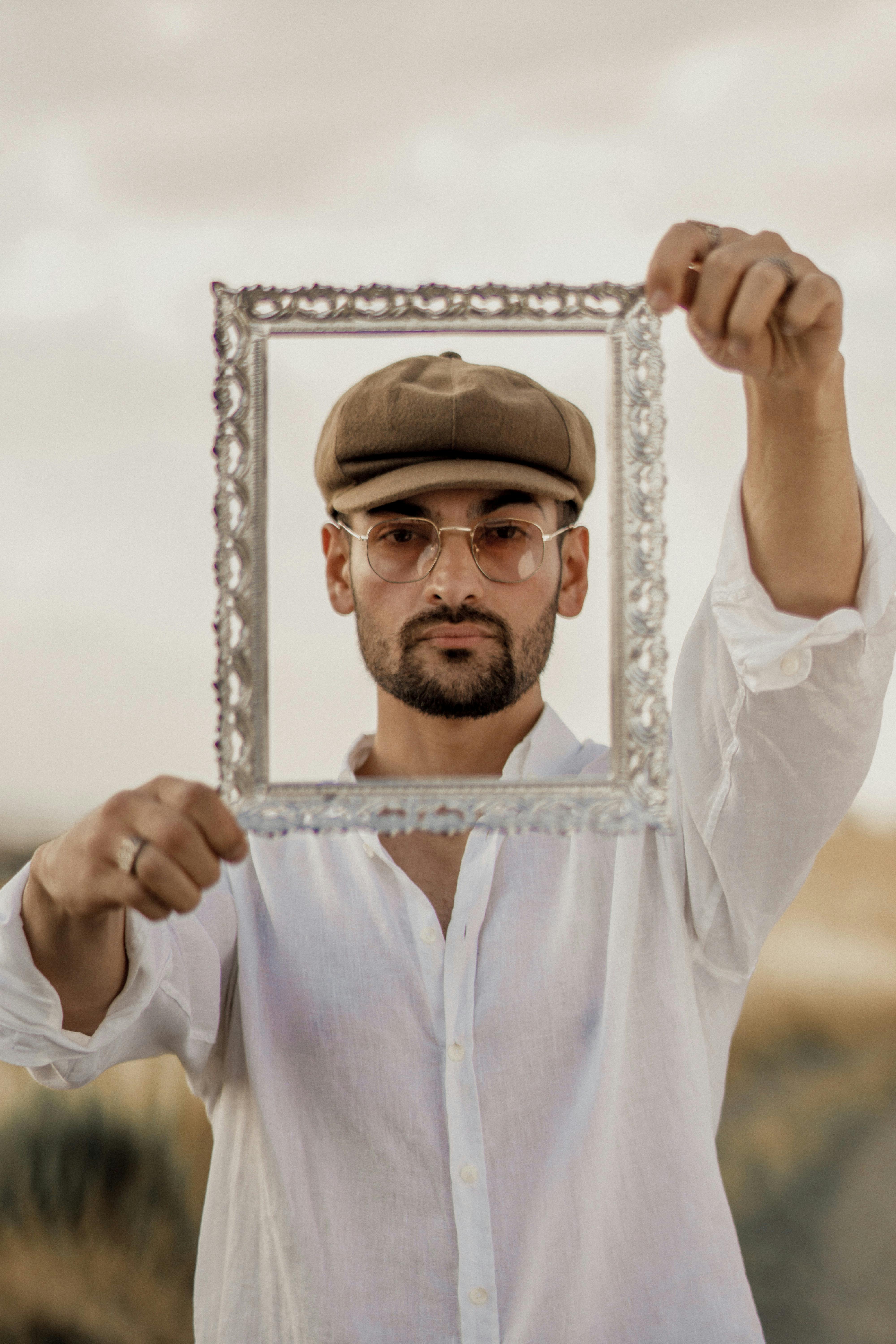 Portrait of a stylish man holding a frame outdoors, blending retro fashion with modern aesthetics.