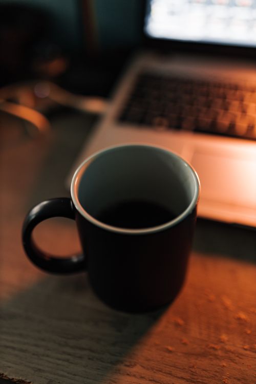 Free A warm, moody setting of a coffee cup on a desk next to a laptop, evoking a cozy work atmosphere. Stock Photo