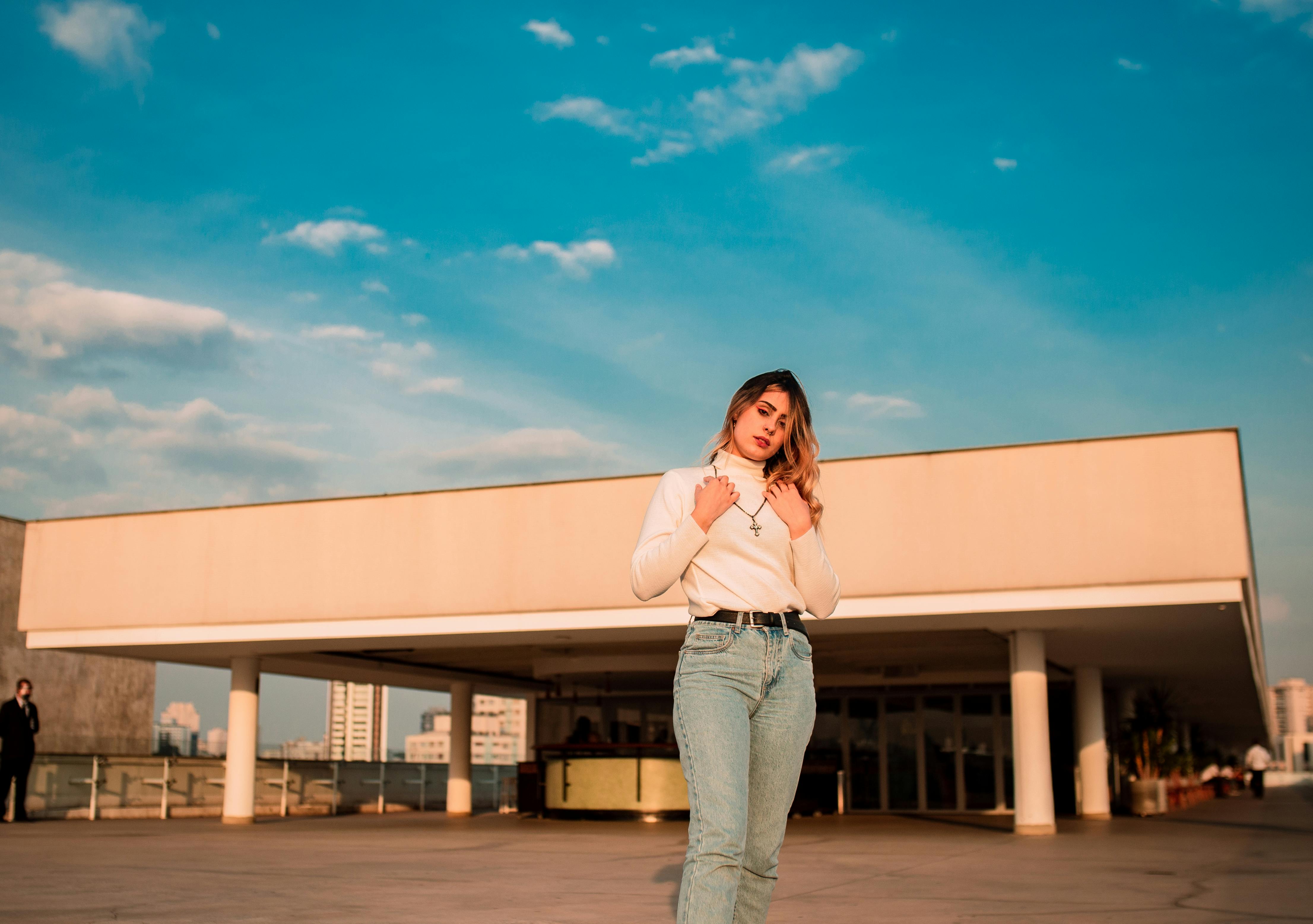 Free Fashionable woman standing in front of a building with a blue sky background. Perfect for urban lifestyle concepts. Stock Photo