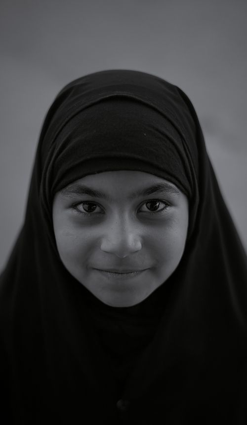 Free A black and white portrait of a young girl smiling in a hijab, conveying warmth and innocence. Stock Photo