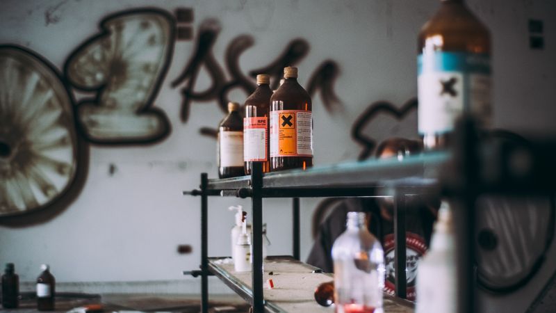Discover an abandoned industrial room featuring shelves of toxic chemical bottles and graffiti walls.
