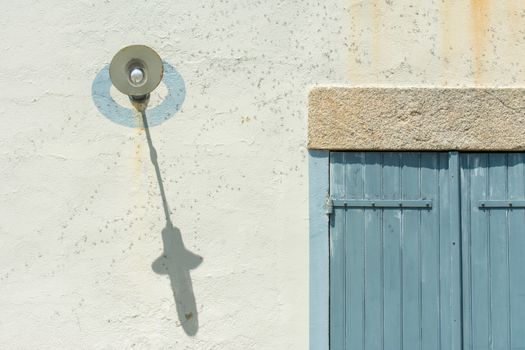 A vintage light fixture casts a shadow on a rustic wall with a blue wooden shutter.