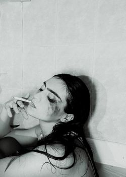 Melancholic portrait of a woman in a bathtub, cigarette in hand, depicting emotional distress.