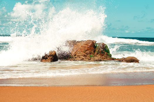 Vibrant scene of waves splashing onto a rocky seashore under a bright summer sky.