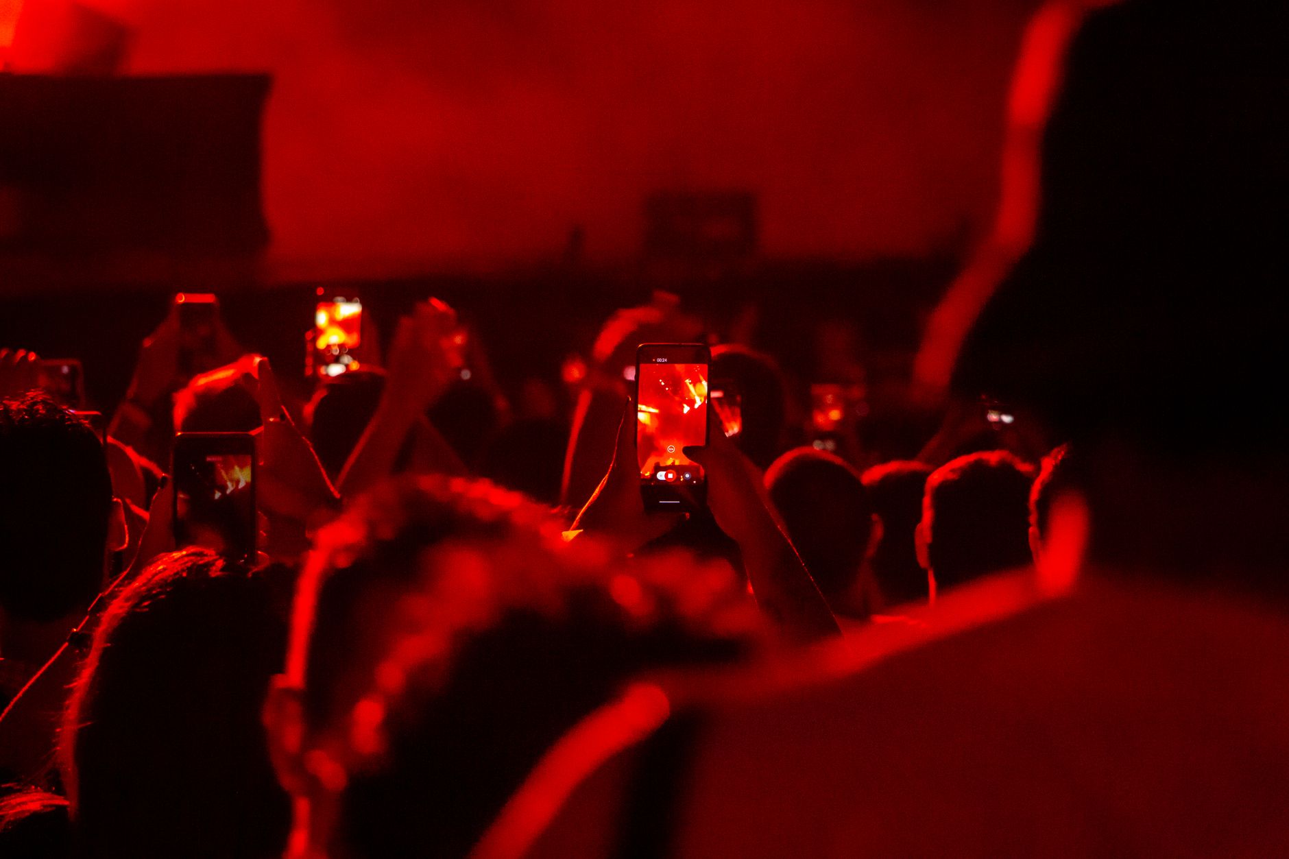 Concert attendees in São Paulo capturing performances with smartphones in a vivid red atmosphere.