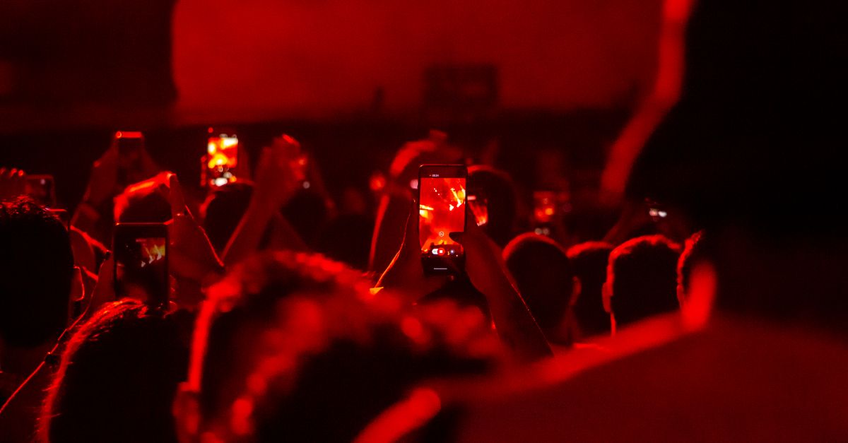 Fãs de concertos em São Paulo registrando apresentações com smartphones em uma atmosfera vermelha vibrante.