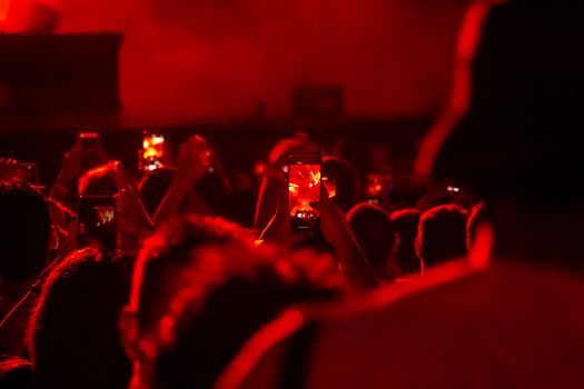 Concert attendees in São Paulo capturing performances with smartphones in a vivid red atmosphere.
