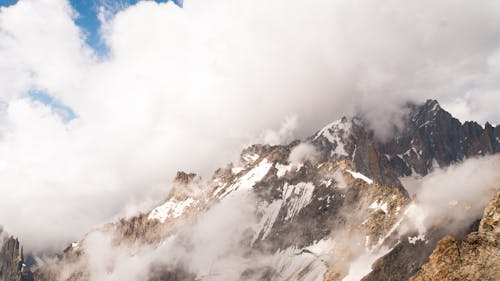 A person standing on top of a mountain with clouds in the sky