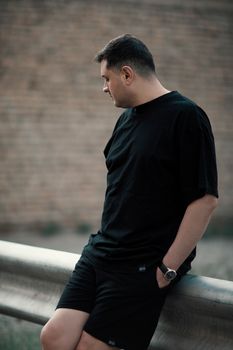 A thoughtful man in black casual attire leans against a rail outdoors in Los Angeles.