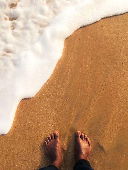 Free Warm ocean waves gently lap against bare feet on a sandy beach, evoking feelings of relaxation and vacation. Stock Photo