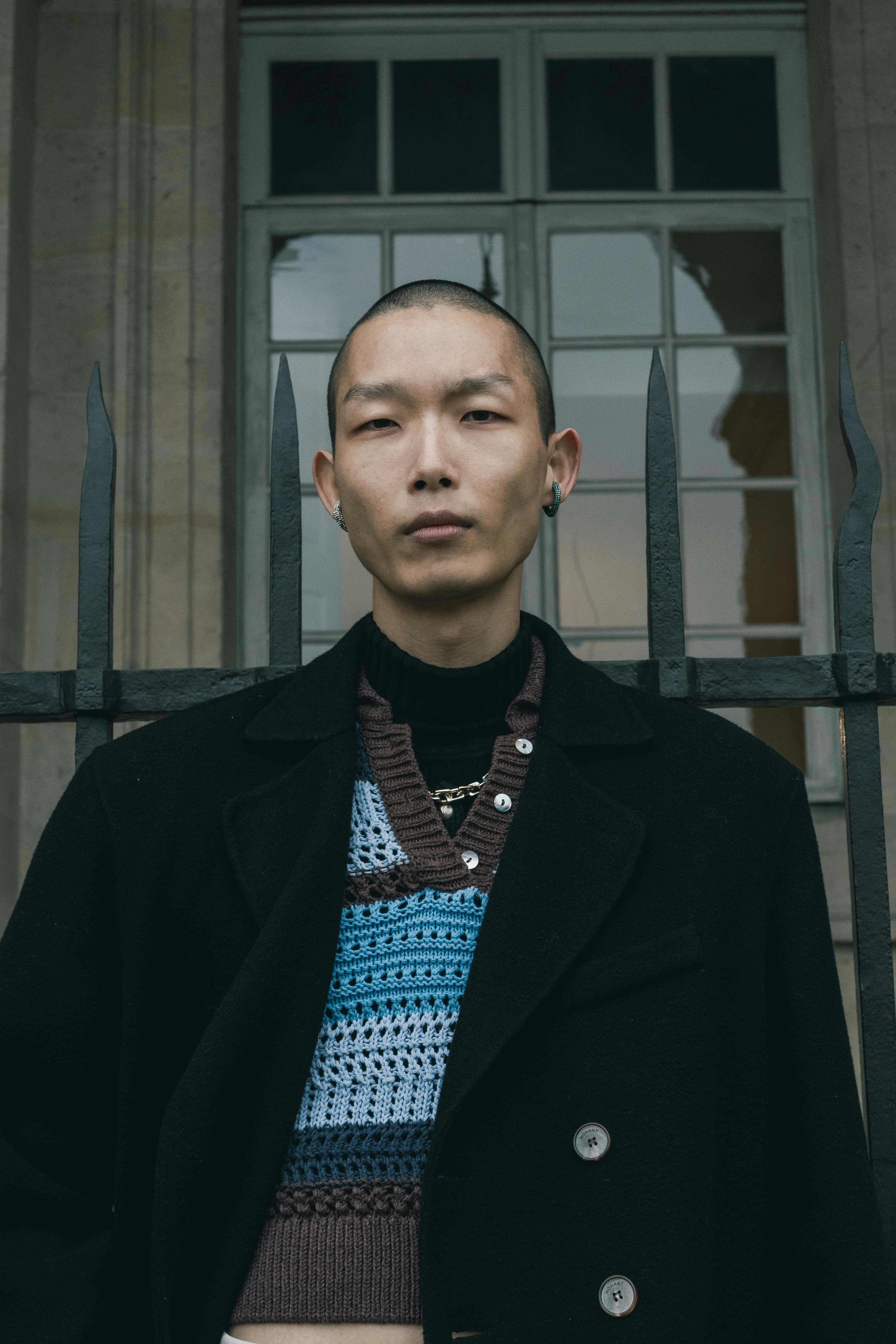 Fashion portrait of an Asian man standing outdoors with a modern urban vibe.