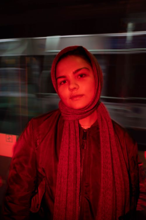 Free A woman in a scarf stands in a metro station lit by red lights, creating a moody urban scene. Stock Photo