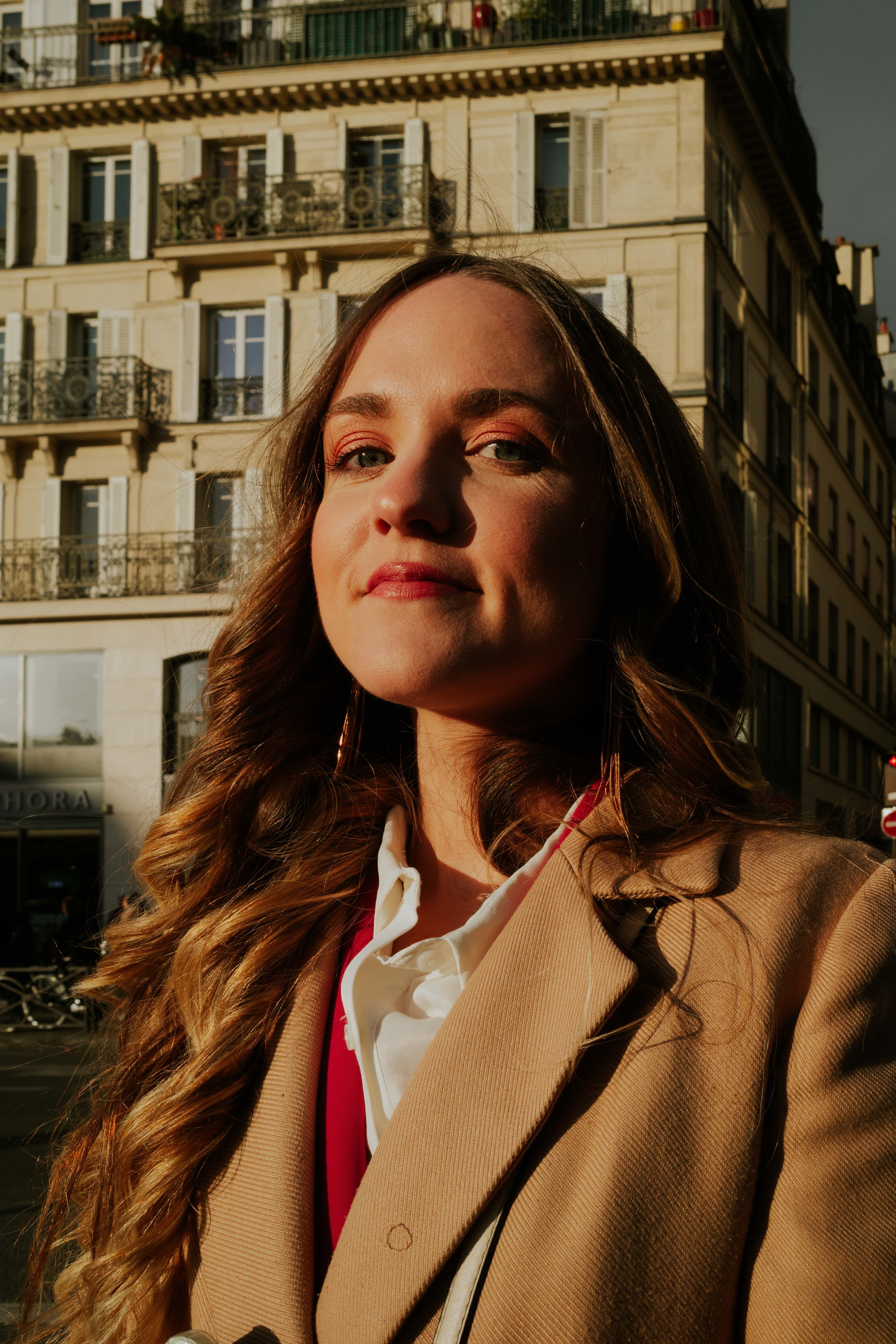 Confident woman poses in city sunlight against historic building backdrop.