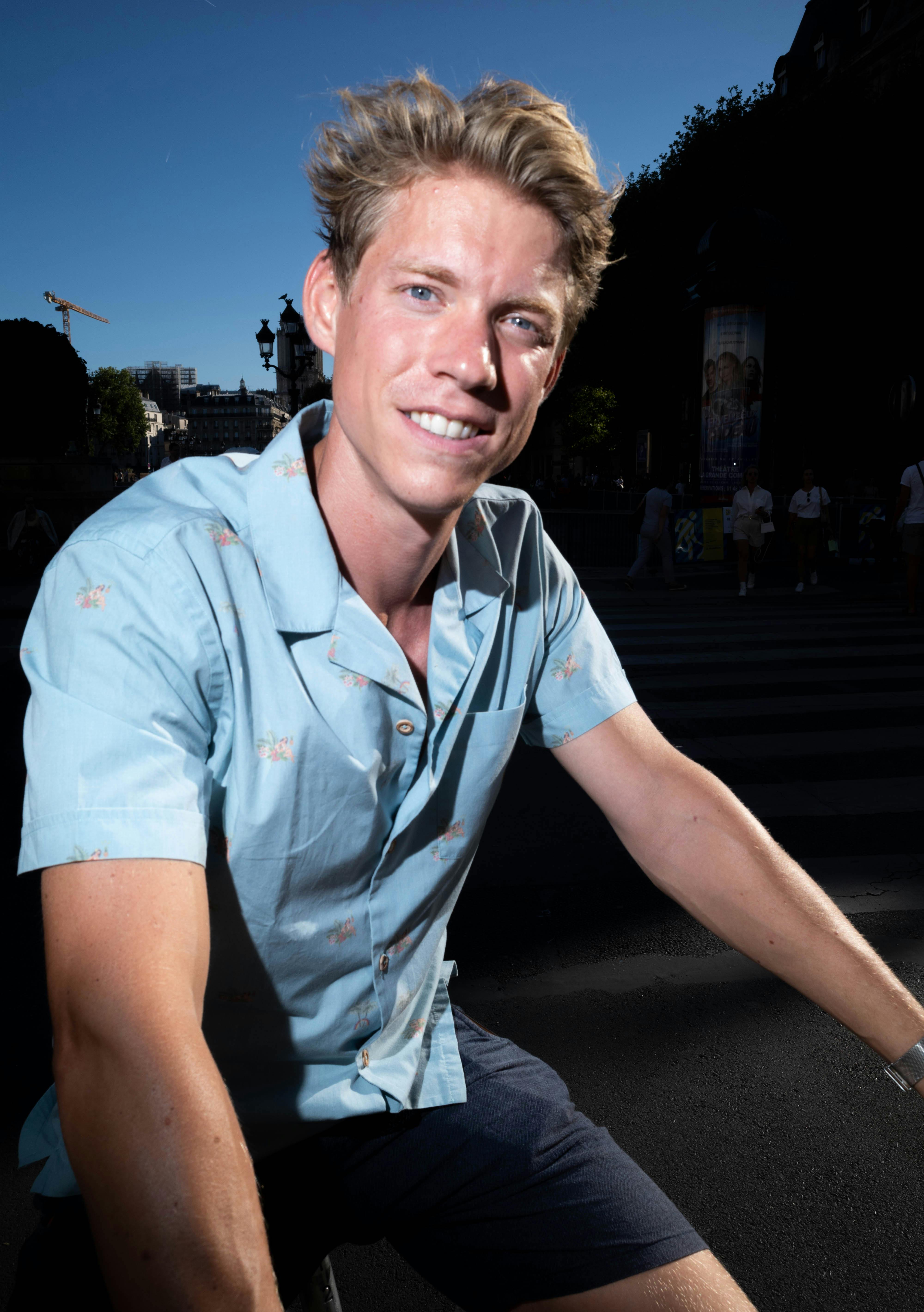 Smiling young man enjoying a sunny day outdoors with urban background.