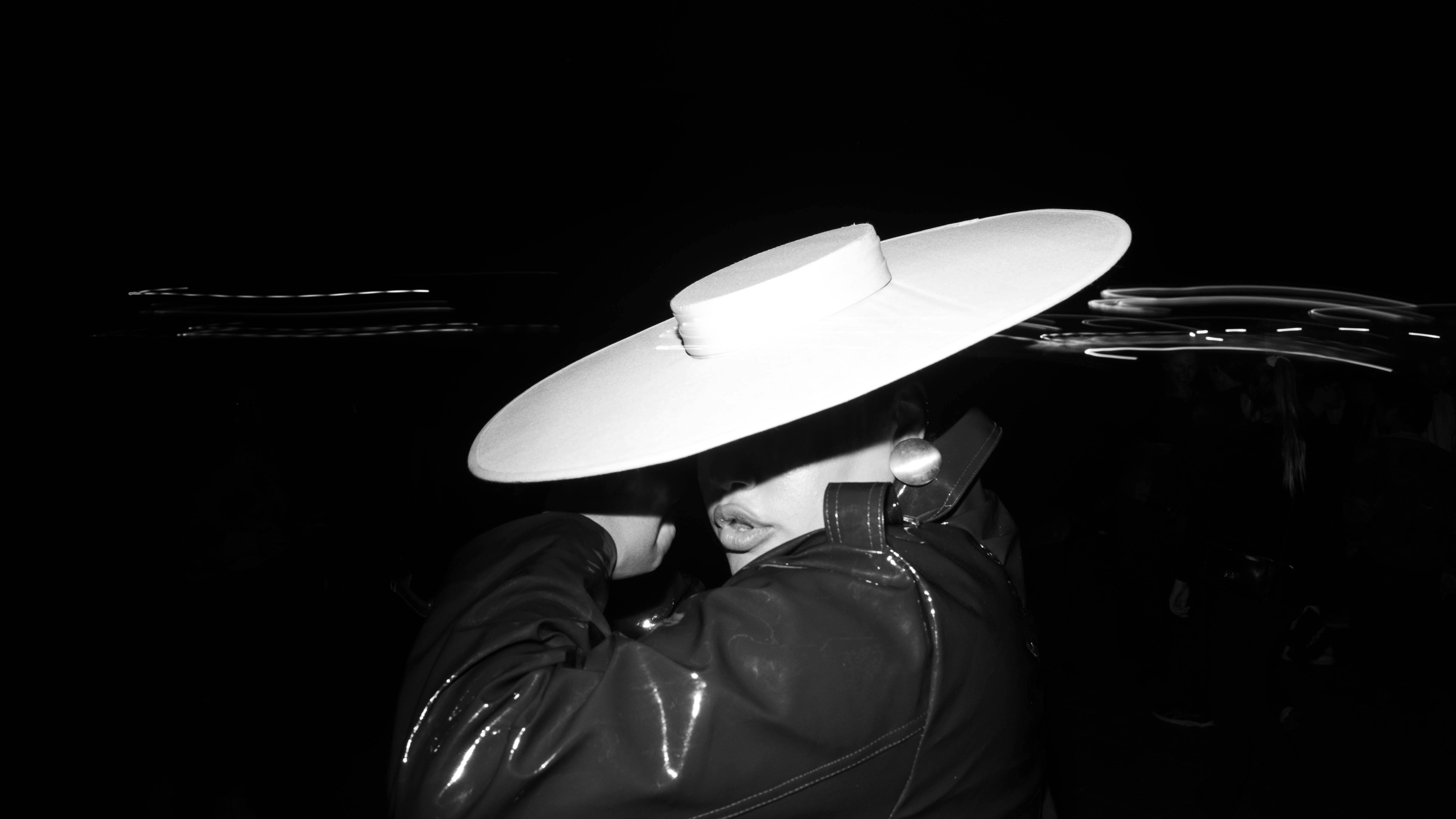 Dramatic black and white portrait of a woman wearing a wide-brimmed hat and leather jacket.
