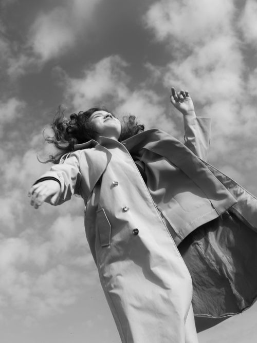 Free Black and white image of a woman joyfully leaping beneath a cloud-filled sky. Stock Photo