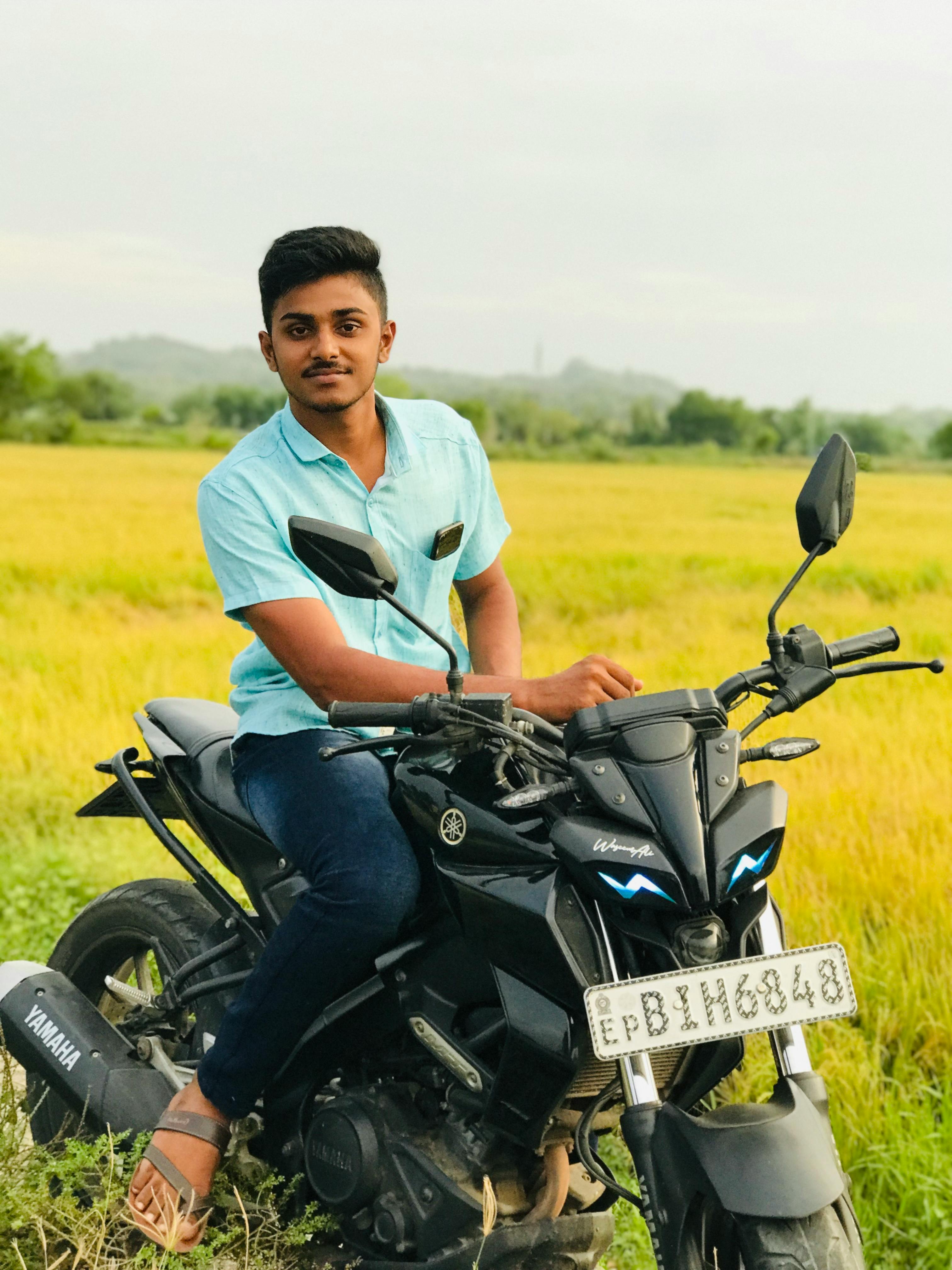 A young man sitting on a motorcycle in a scenic countryside field during the day.